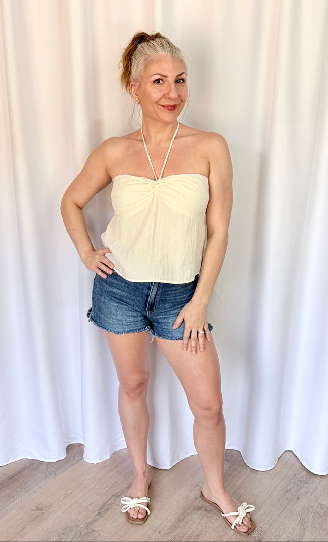 Woman wearing a strapless top and denim shorts against a white curtain background