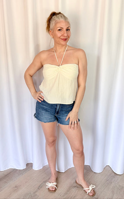 Woman wearing a strapless top and denim shorts against a white curtain background