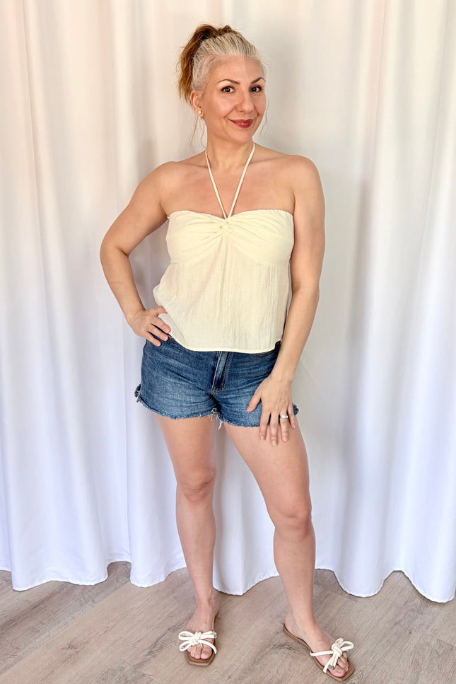Woman wearing a strapless top and denim shorts against a white curtain background