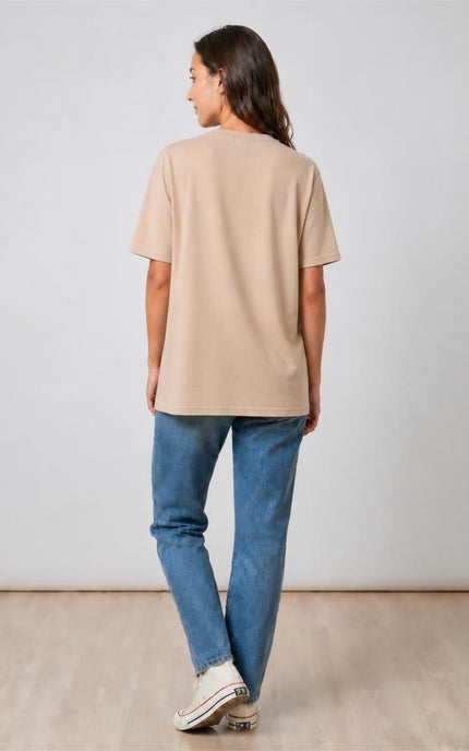 Person wearing a beige t-shirt and blue jeans standing against a plain background