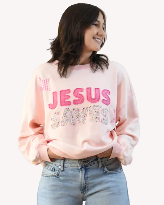 Person wearing a pink sweatshirt with 'Jesus' printed on it, standing against a plain background.
