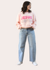 Person wearing a pink 'Jesus Loves Me' sweatshirt and light blue jeans indoors.