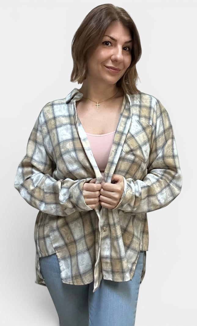 A woman wearing a light beige and white plaid button-up shirt over a light pink top and blue jeans, standing against a plain light gray background.
