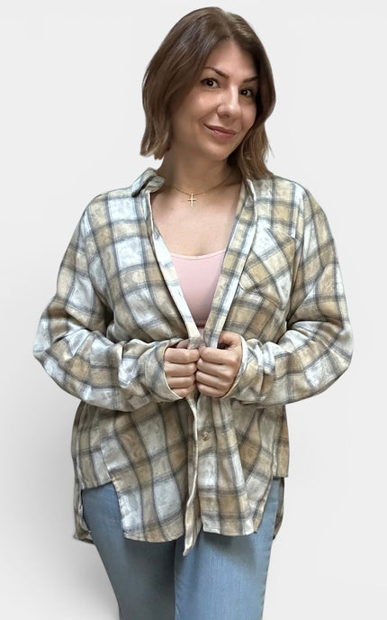 A woman wearing a light beige and white plaid button-up shirt over a light pink top and blue jeans, standing against a plain light gray background.