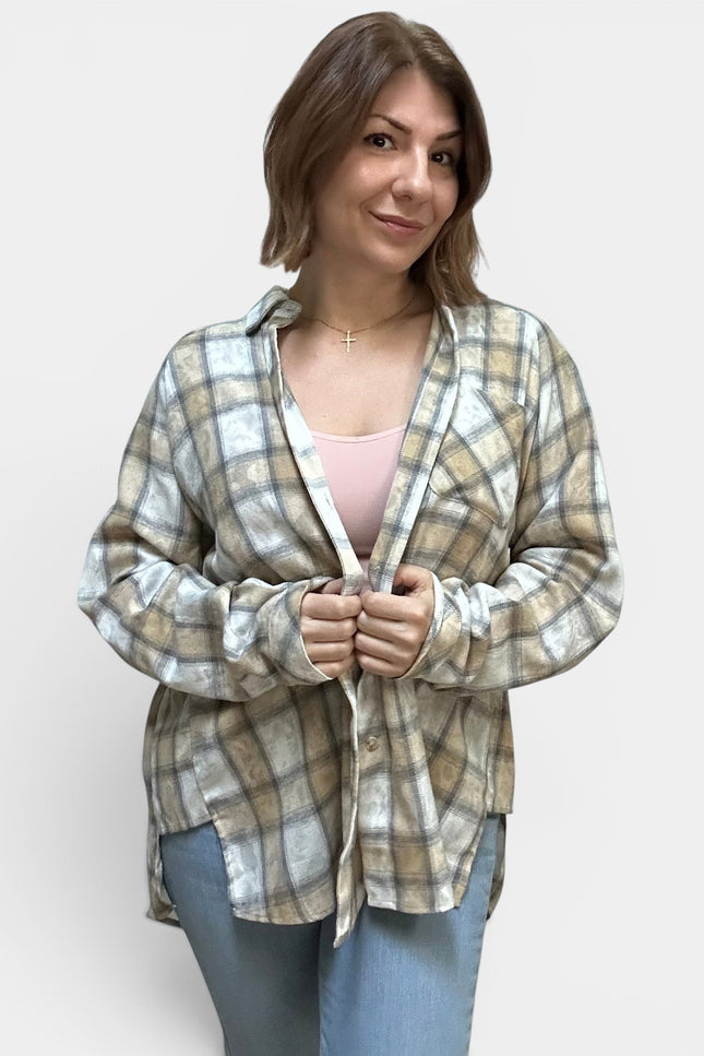 A woman wearing a light beige and white plaid button-up shirt over a light pink top and blue jeans, standing against a plain light gray background.