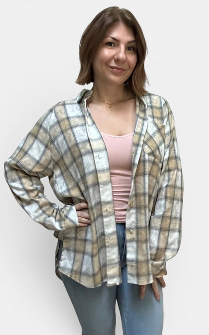 A woman modeling a long-sleeve plaid button-up shirt in beige, white, and gray, worn open over a light pink tank top and blue jeans, against a plain light gray background.