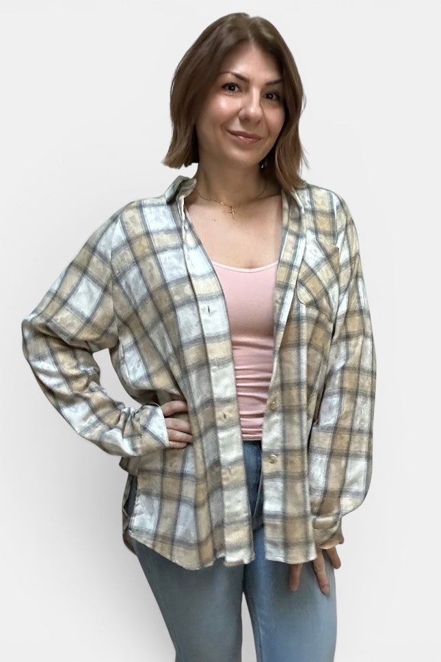 A woman modeling a long-sleeve plaid button-up shirt in beige, white, and gray, worn open over a light pink tank top and blue jeans, against a plain light gray background.