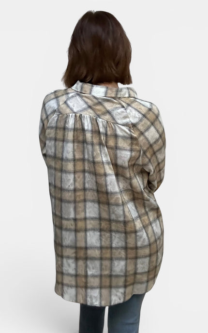 A woman viewed from behind wearing a long-sleeve plaid button-up shirt in beige, brown, and white, paired with blue jeans, against a plain light gray background.
