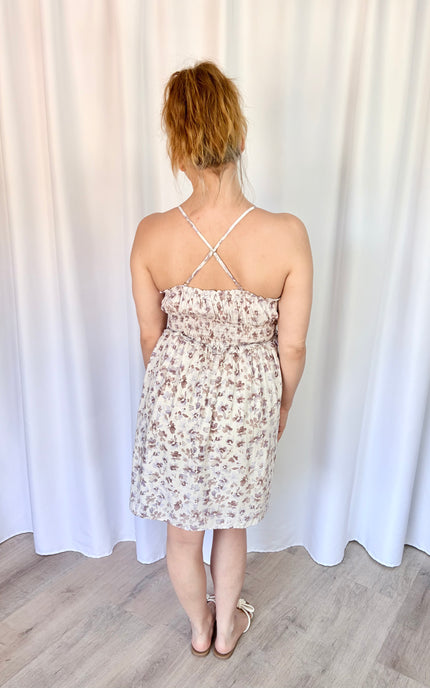Back view of a lavender floral mini dress featuring a smocked back, tie detail, and pockets.