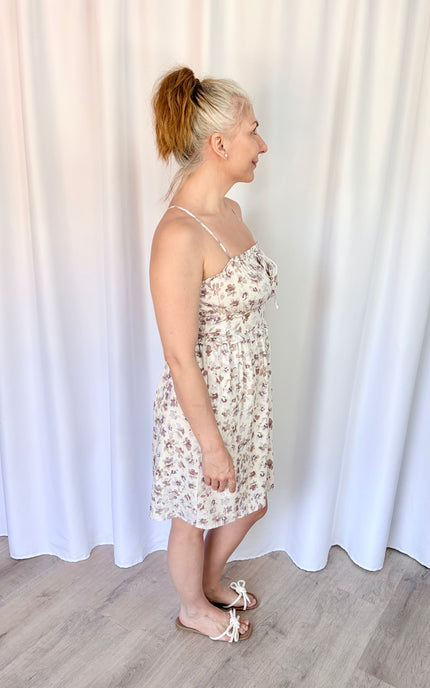 Right side view of a lavender floral mini dress featuring a smocked back, tie detail, and pockets.