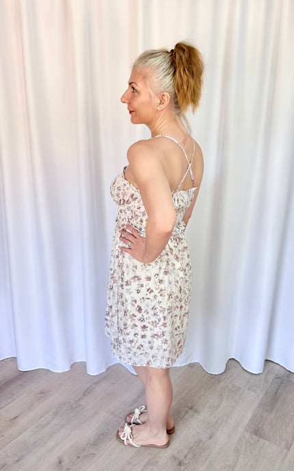 Side view of a lavender floral mini dress featuring a smocked back, tie detail, and pockets.