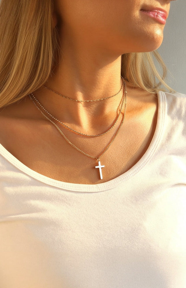 Three‑layer 18k gold PVD necklace featuring chains of varying lengths and a small cross pendant, hypoallergenic stainless steel design.