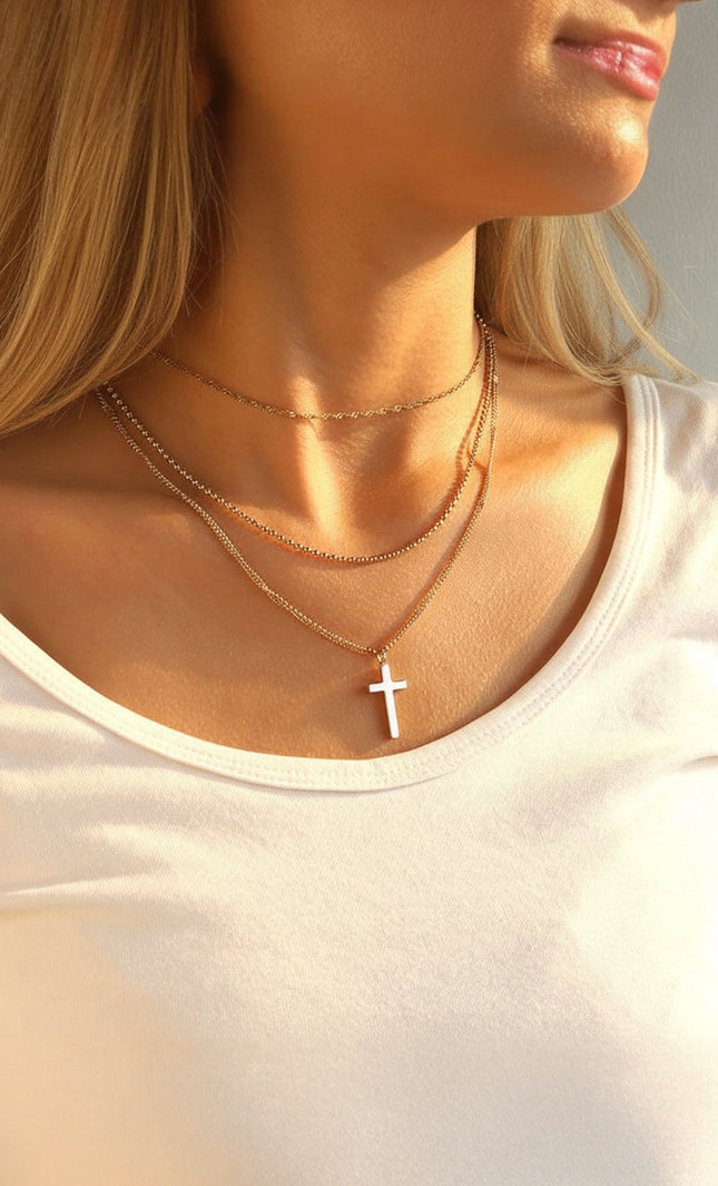 Three‑layer 18k gold PVD necklace featuring chains of varying lengths and a small cross pendant, hypoallergenic stainless steel design.