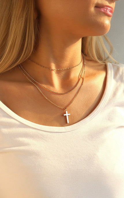 Three‑layer 18k gold PVD necklace featuring chains of varying lengths and a small cross pendant, hypoallergenic stainless steel design.