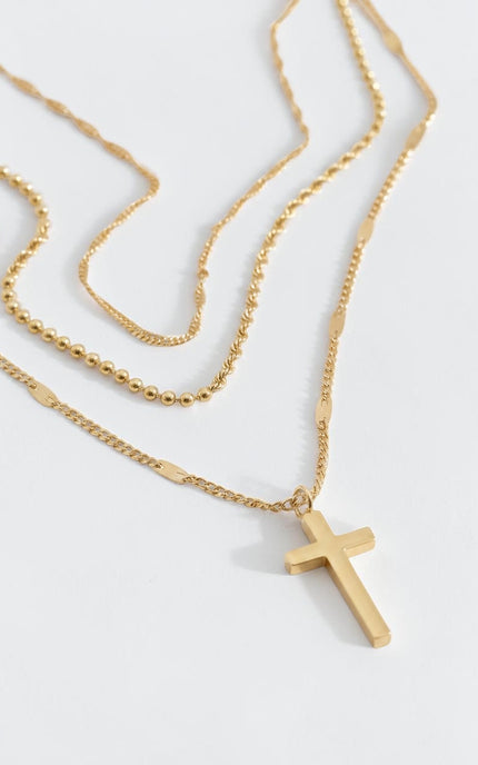 Layered gold triple‑chain necklace with a small cross pendant, 18k gold PVD stainless steel, waterproof and hypoallergenic.