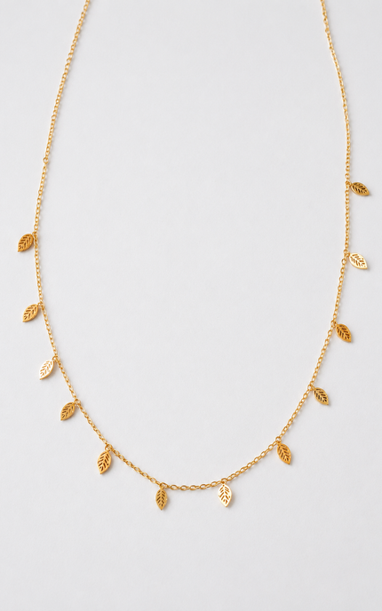 A delicate gold chain necklace featuring small, textured leaf-shaped charms hanging along the front, displayed against a clean, light gray background.