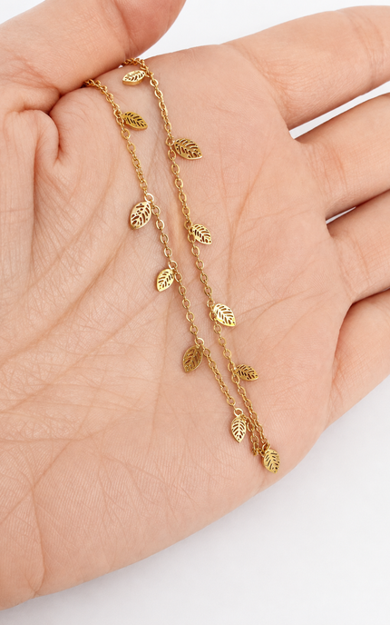 A delicate gold leaf chain bracelet draped across a person's palm, showcasing the fine details of the small leaf charms on the chain.