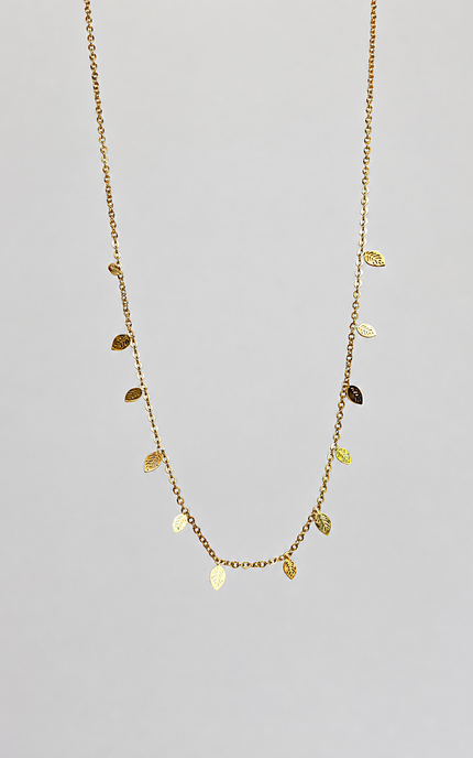 A delicate gold chain necklace featuring small, textured leaf-shaped charms in varying shades of gold, displayed against a solid light gray background.