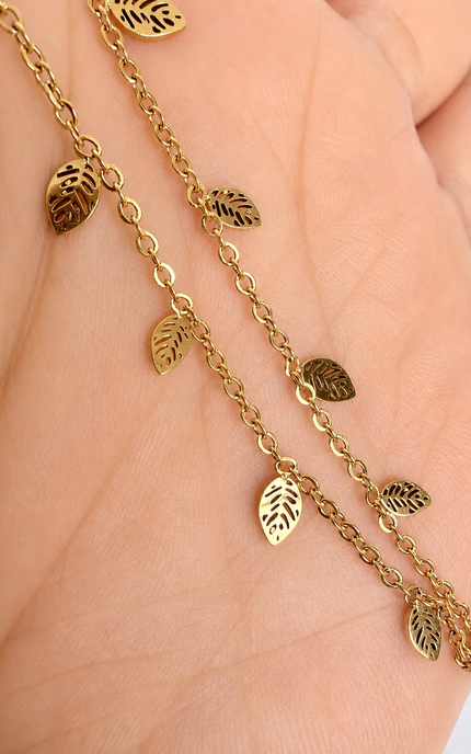 A gold-toned chain bracelet with small leaf-shaped charms, shown draped across a person's hand.