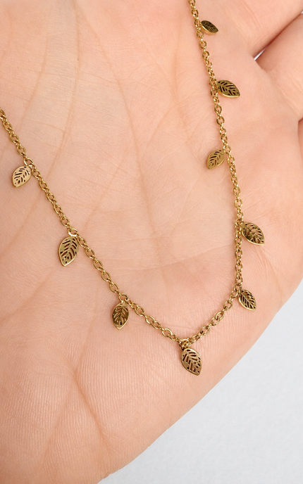 A delicate gold leaf chain necklace draped across a person's palm, showing small leaf-shaped charms on a fine chain.