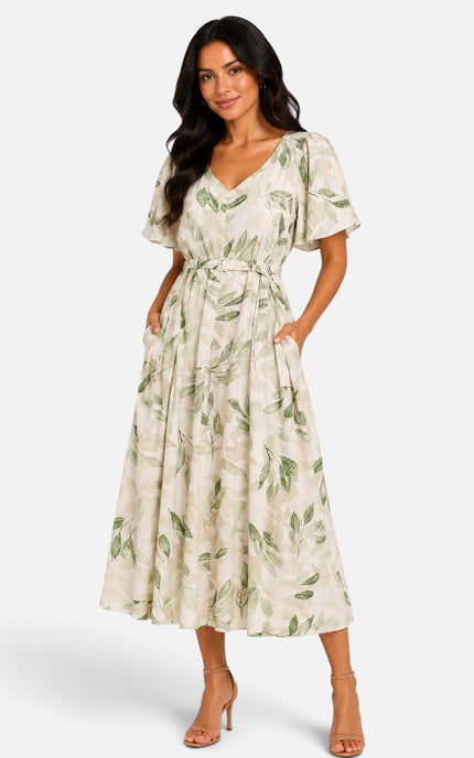 A woman modeling a cream-colored midi dress with a green leaf pattern, featuring short flutter sleeves, a V-neckline, and a matching fabric tie belt at the waist, set against a plain light gray studio background.