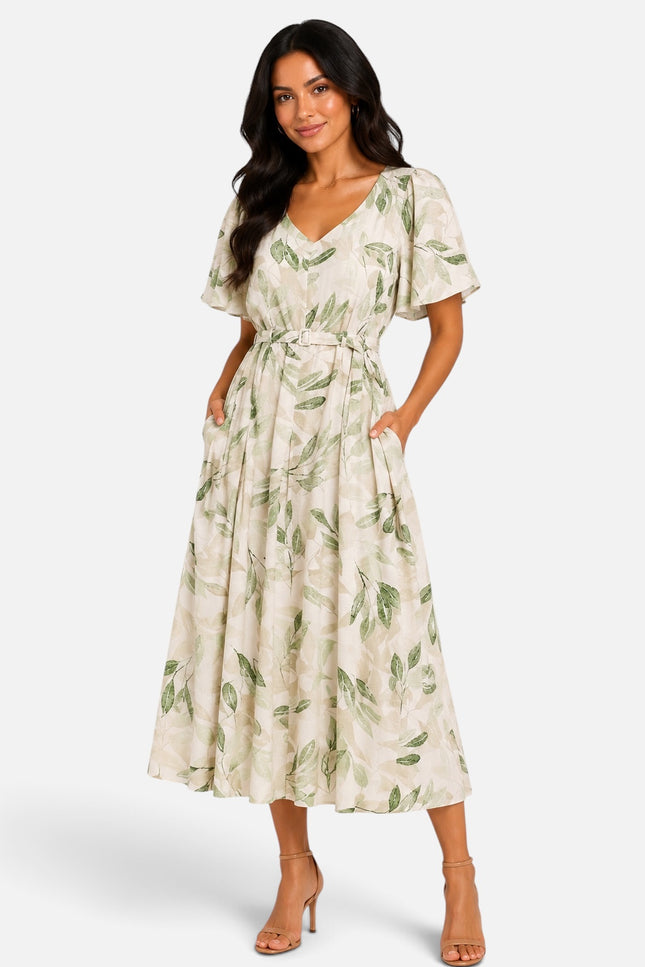 A woman modeling a cream-colored midi dress with a green leaf pattern, featuring short flutter sleeves, a V-neckline, and a matching fabric tie belt at the waist, set against a plain light gray studio background.