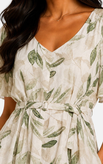A close-up of a woman wearing a cream-colored wrap-style dress with a green leaf print and a matching tie belt.