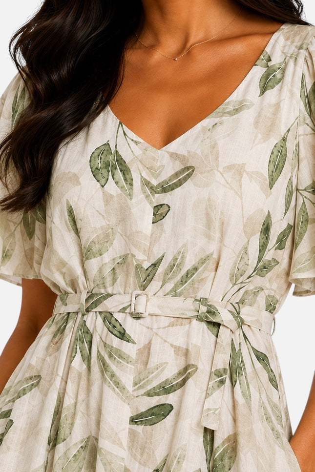 A close-up of a woman wearing a cream-colored wrap-style dress with a green leaf print and a matching tie belt.