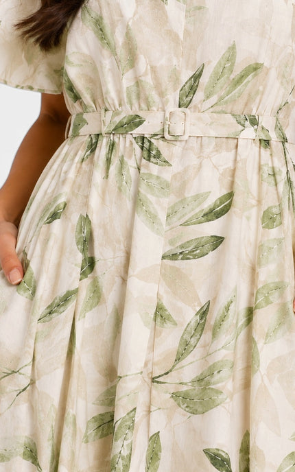 Close-up of a cream-colored dress with a green leaf print pattern, featuring a matching fabric belt with a silver buckle and side pockets.