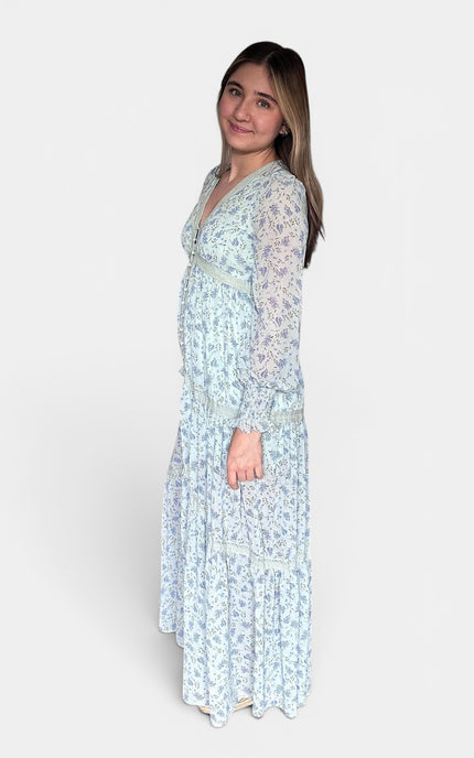 Light blue and white floral maxi dress with sheer long sleeves, shown from a side profile against a plain light gray studio background.