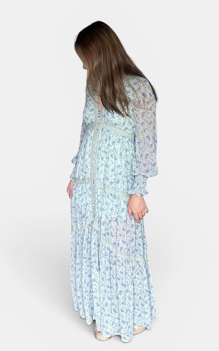 Long-sleeved maxi dress with a light blue and white floral pattern, shown from a side-back angle against a plain light gray studio background.
