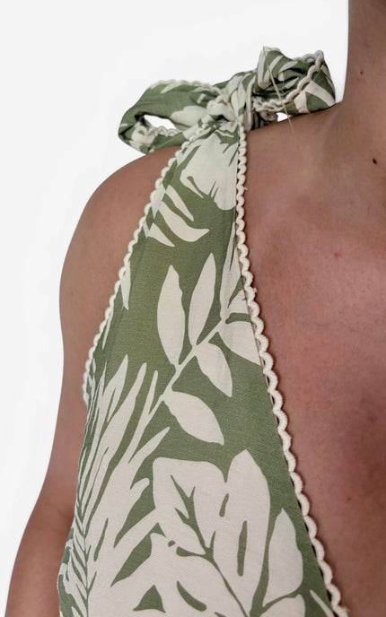 Close-up of a model wearing a green and white tropical leaf print halter top with a tie-neck detail and scalloped edges.