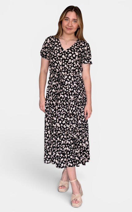 Short-sleeve midi dress with a black background and a dense white floral pattern, paired with beige platform sandals, against a plain light gray studio background.