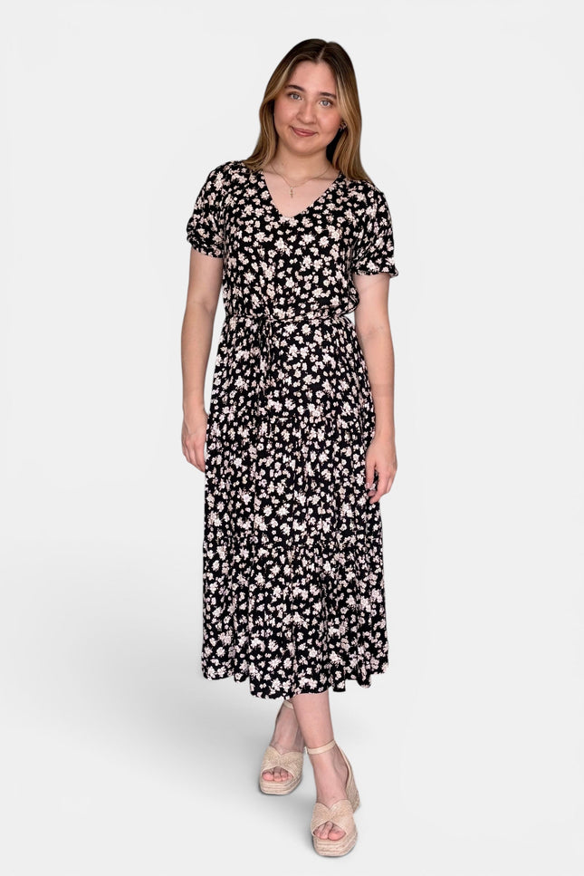 Short-sleeve midi dress with a black background and a dense white floral pattern, paired with beige platform sandals, against a plain light gray studio background.