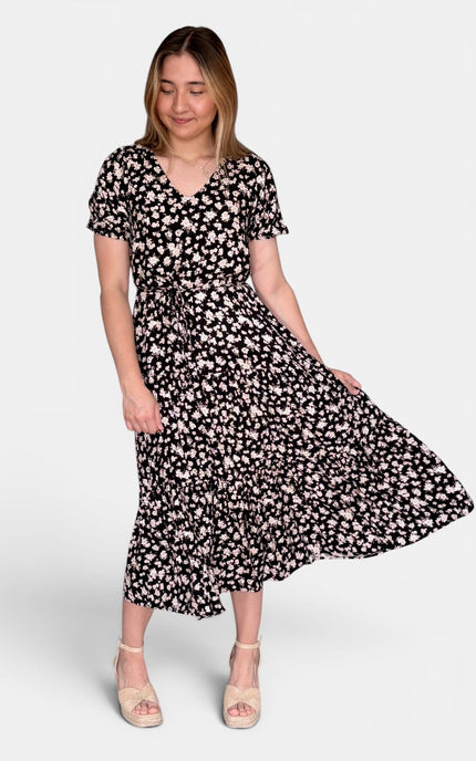 Short-sleeve midi dress with a black base and white floral print, paired with beige heeled sandals, against a light gray studio background.