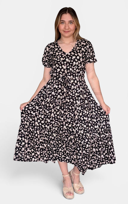 Black midi dress with a dense white floral print, featuring short sleeves, a V-neckline, and a self-tie waist, set against a plain light gray background.