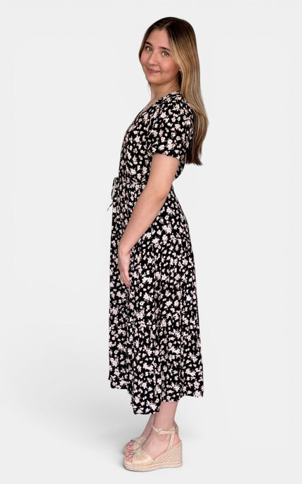 Side view of short-sleeve midi dress with a black background and a white floral pattern, shown from a side-back angle against a light gray studio background.