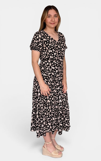 Short-sleeve midi dress with a black base and a dense white floral pattern, paired with beige wedge sandals, against a light gray studio background.