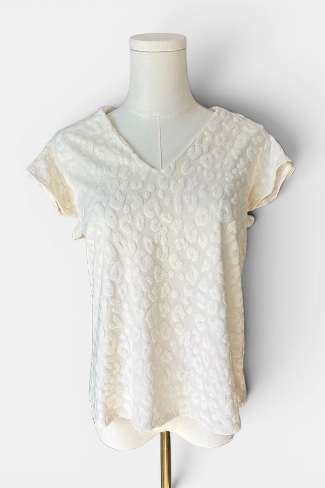 An off-white textured short-sleeve top with a V-neckline, displayed on a cream-colored mannequin torso against a light gray background.
