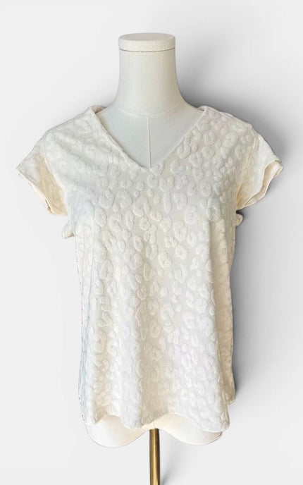An off-white textured short-sleeve top with a V-neckline, displayed on a cream-colored mannequin torso against a light gray background.