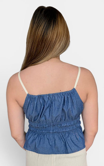 Back of camisole top with thin cream straps and a gathered waist, paired with light beige bottoms, against a plain light gray studio background.
