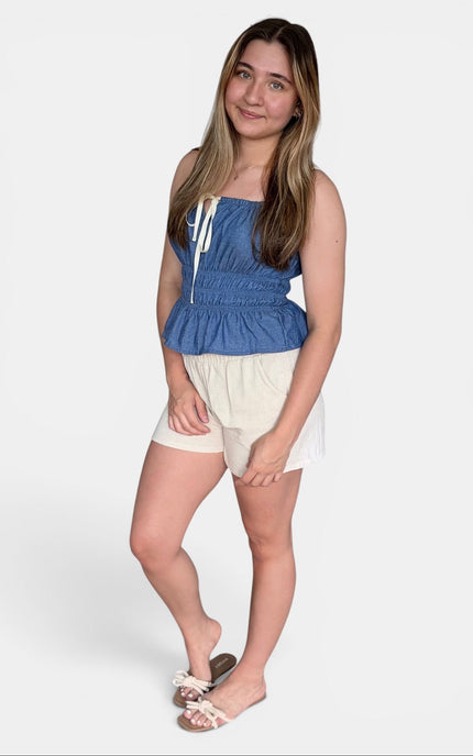 Blue strapless peplum top with white drawstrings and cream shorts against a light gray studio background.