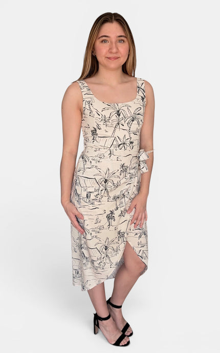 A sleeveless midi dress with a black line-art tropical and beach-themed print on a warm cream background, paired with black strappy heels, against a light gray studio background.