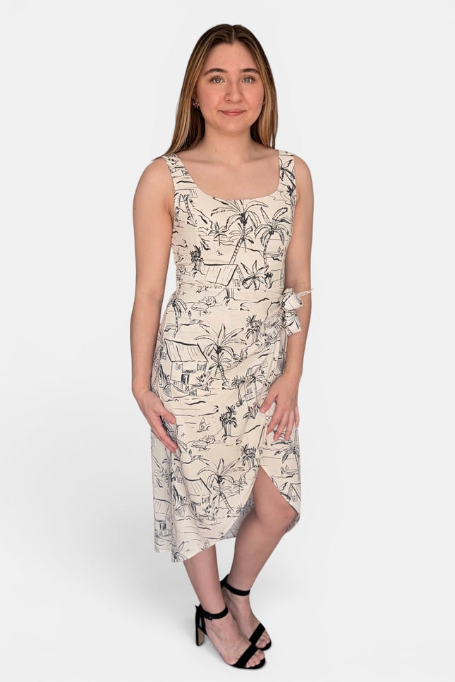 A sleeveless midi dress with a black line-art tropical and beach-themed print on a warm cream background, paired with black strappy heels, against a light gray studio background.