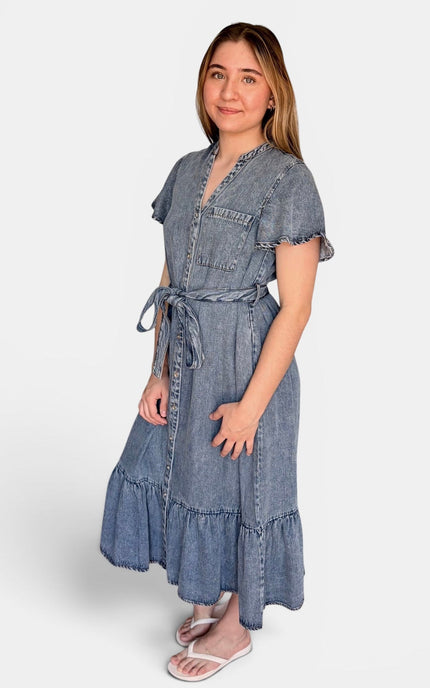Short-sleeve denim midi dress with a tie waist and ruffled hem, standing against a light gray studio background.