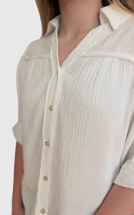 Close-up of a person wearing a short-sleeve textured button-front shirt in a warm off-white or cream tone, with visible wood-tone buttons and a collar.