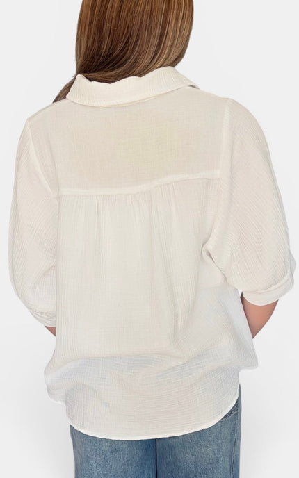 A woman viewed from the back wearing a textured off-white short-sleeve blouse and blue jeans against a plain white background.