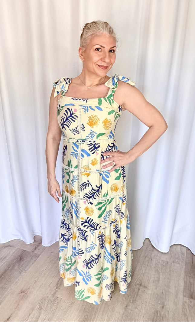 Front view of a model wearing the full-length Marina Maxi Dress in a vibrant reef print, showcasing its square folded neckline, wide adjustable tie straps, and a flowing skirt with intricate tiered ladder trim.