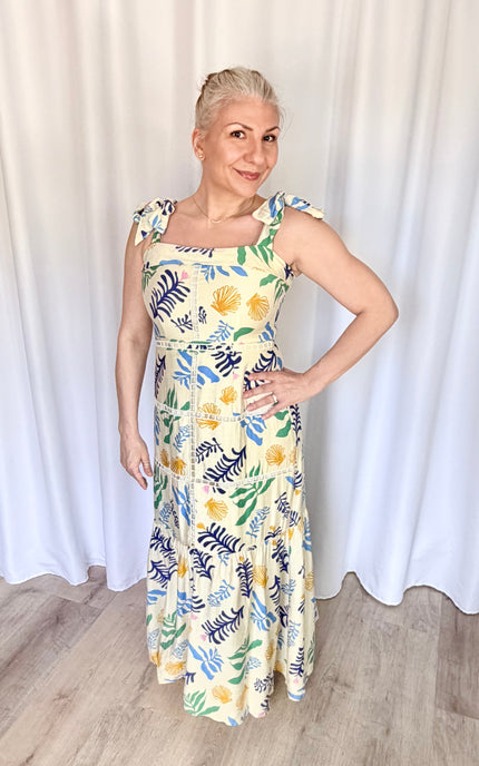 Front view of a model wearing the full-length Marina Maxi Dress in a vibrant reef print, showcasing its square folded neckline, wide adjustable tie straps, and a flowing skirt with intricate tiered ladder trim.