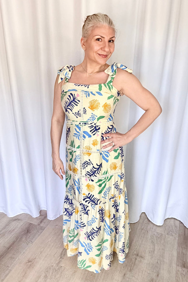 Front view of a model wearing the full-length Marina Maxi Dress in a vibrant reef print, showcasing its square folded neckline, wide adjustable tie straps, and a flowing skirt with intricate tiered ladder trim.